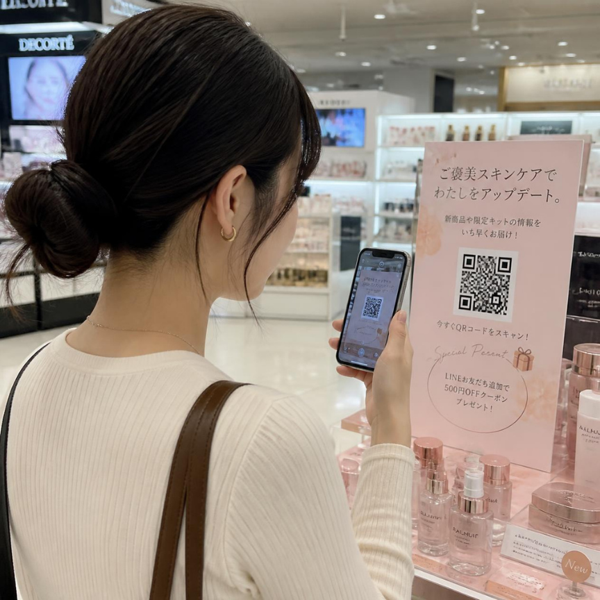 化粧品売場のPOPからQRコードを読み取る来店客